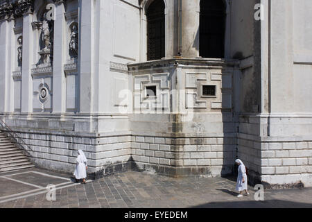 Deux religieuses à pied dans la chaleur de l'après-midi sous les murs de l'église Santa Maria della Salute à Dorsoduro, district de Venise, Italie. Banque D'Images