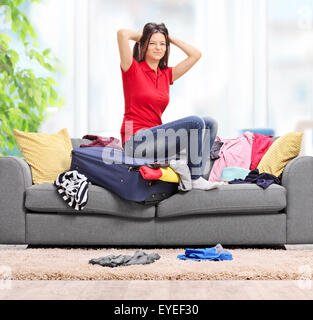 Les jeunes en colère femme assise sur sa valise à la maison et essayer de s'adapter tous ses vêtements en feu dans l'objectif de décentrement et Banque D'Images