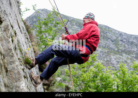 Novice senior male rock climber abseiling avec corde de sécurité sur un rocher. Ogwen, Snowdonia, le Nord du Pays de Galles, Royaume-Uni, Angleterre Banque D'Images