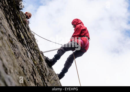 Female rock climber abseiling down un rocher avec une corde sur un rocher belayed à partir de ci-dessus. Snowdonia, le Nord du Pays de Galles, Royaume-Uni, Angleterre Banque D'Images