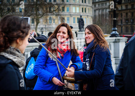 Deux jeunes amies en tenant vos autoportraits à l'aide de bâton selfies, Trafalgar Square, London, UK Banque D'Images
