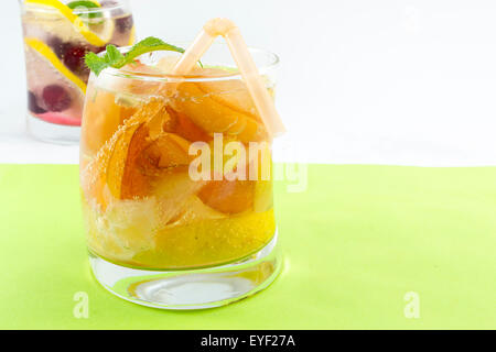 Cocktail de jus de pêche avec des tranches de pêches dans un verre de travers sur fond vert Banque D'Images