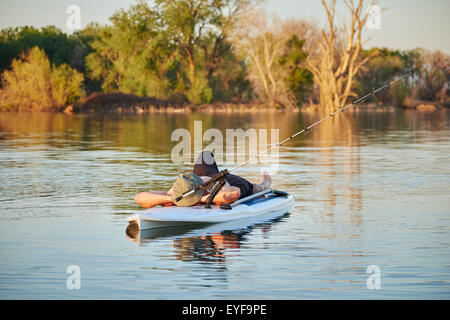 Un jeune homme nu portant un chapeau de dormir sur un paddle board alors que la pêche sur un petit lac sur une chaude journée d'été dans le Nord de la Californie Banque D'Images