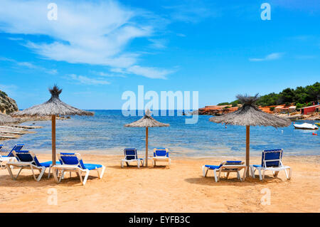 Chaises longues et parasols dans le rustique es pou des Lleo Cove dans l'île d'Ibiza, Espagne, et ses abris de pêcheurs traditionnels Banque D'Images