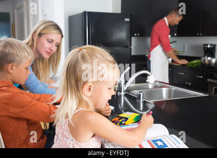 Mère fait ses devoirs avec son (10-11) et sa fille (2-3) et le père preparing meal Banque D'Images