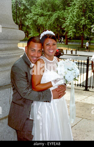 Un heureux Hispanic Bride and Groom hug sur le trottoir après avoir été mariés dans une cérémonie civile à Mariage du greffier de la ville Bureau à New York City. Remarque suite nuptiale robe et bouquet. Banque D'Images