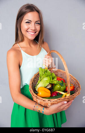 Portrait of a smiling woman holding basket avec des légumes sur fond gris Banque D'Images