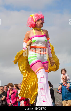 Carnaval de Swanage Procession en juillet avec le thème de super-héros - sur des échasses. Femme personne debout sur pilotis. Banque D'Images