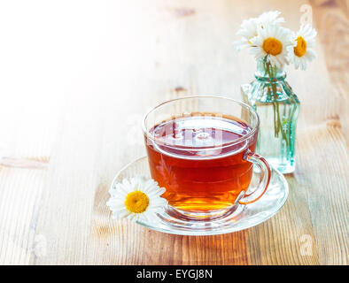Tasse de thé en verre avec fleurs de camomille sur fond de bois rustique Banque D'Images