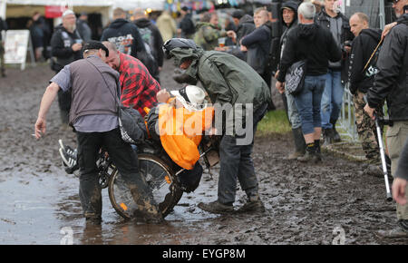 Le Wacken, Allemagne. 29 juillet, 2015. Les visiteurs du W.O.A. (Wacken Open Air) Pousser un utilisateur de fauteuil roulant dans la boue sur le site du festival au Wacken, Allemagne, 29 juillet 2015. Heavy metal fans de partout dans le monde viennent à Wacken à célébrer le plus grand festival de heavy metal. Dpa : Crédit photo alliance/Alamy Live News Banque D'Images