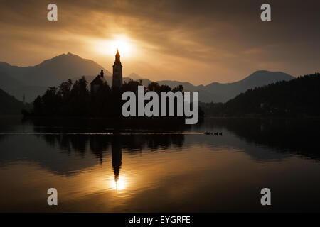 Lever de Soleil sur le lac de Bled et l'église de l'île de l'assomption de Marie avec le massif des Karavanke montagnes en arrière-plan, slovène Banque D'Images