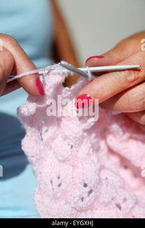 Une femme à l'aide d'aiguilles à tricoter un cardigan en laine rose à l'aide d'une couture purl Banque D'Images
