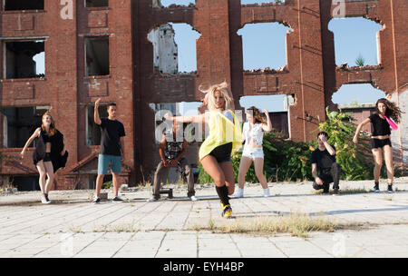 Jeune fille danse hip hop dans une place urbaine avec ses amis son appui. La lumière naturelle par le soleil sur les immeubles de grande hauteur. Banque D'Images