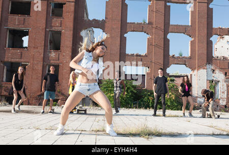 Jeune fille danse hip hop dans une place urbaine avec ses amis son appui. La lumière naturelle par le soleil sur les immeubles de grande hauteur. Banque D'Images