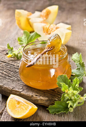 Confiture de melon dans un bocal en verre, des tranches de citron, melon sur un fond de bois Banque D'Images