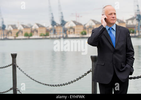 Businessman wearing costume foncé, parler sur son téléphone portable et situé à les Docklands de Londres. Banque D'Images