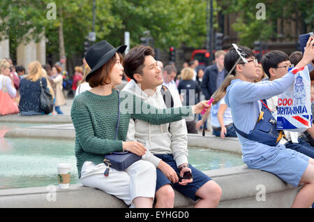 Londres, Angleterre, Royaume-Uni. Jeune couple japonais à Trafalgar Square de prendre leur photo avec un bâton selfies Banque D'Images