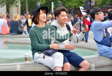 Londres, Angleterre, Royaume-Uni. Jeune couple japonais à Trafalgar Square de prendre leur photo avec un bâton selfies Banque D'Images