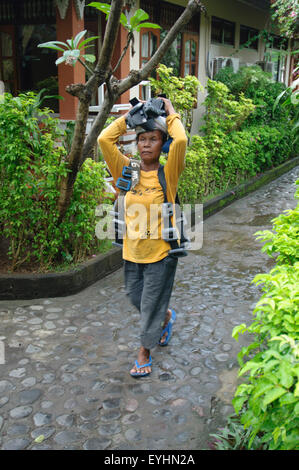 Une vieille femme porter il transporte plusieurs kilogrammes de poids sur ses épaules et la tête, Tulamben, Bali, Indonésie Banque D'Images