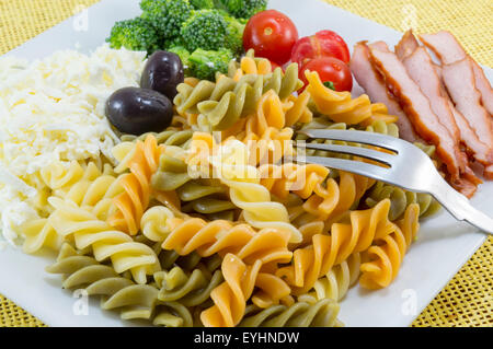 Pâtes de couleur servi sur une plaque blanche avec fromage, olives le brocoli, les tomates cerises et les tranches de viande fumée Banque D'Images