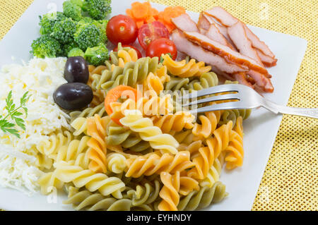 Pâtes de couleur servi sur une plaque blanche avec fromage, olives le brocoli, les tomates cerises et les tranches de viande fumée Banque D'Images
