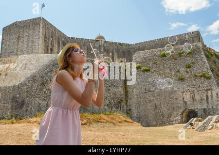 Jeune fille soufflant des bulles de savon à la forteresse portant chapeau de paille et robe rose Banque D'Images