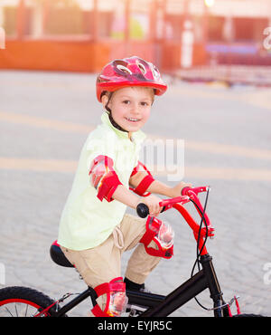 Petit Garçon jouant à l'extérieur, cute cheerful enfant s'amusant dans un camp d'équitation, vélo, élégant rouge sur profiter de l'été Banque D'Images