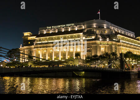 Le Fullerton Hotel sur Singapour éclairé la nuit avec le Cavenagh Bridge au premier plan Banque D'Images