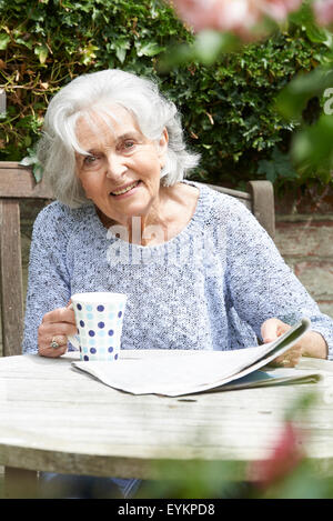 Portrait of Senior Woman Relaxing In Garden Reading Newspaper Banque D'Images