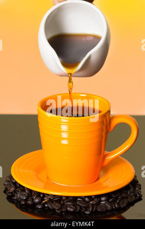 Verser le café de verre blanc électrique dans le quartier coloré de orange mug assis sur le dessus du café en grains et surface brillante Banque D'Images