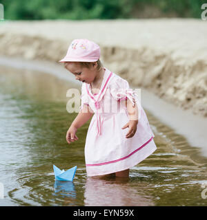 Fille joue avec des bateaux en papier dans la rivière Banque D'Images