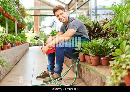 Eau avec jardinier heureux assis entre les plantes dans une pépinière shop Banque D'Images