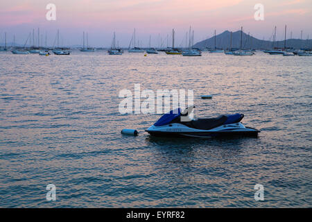 Un Jet Ski garé dans l'eau pour la soirée avec des bateaux, les mâts, les montagnes et le coucher du soleil dans l'arrière-plan Banque D'Images