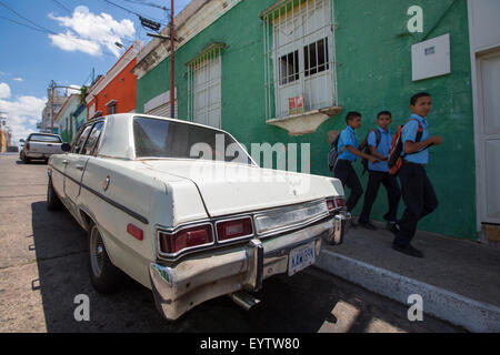 Vieille épave voiture garée dans la vieille ville coloniale de Ciudad Bolivar avec les enfants en revenant de l'école. Le Venezuela Banque D'Images