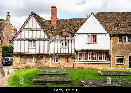 Rue Church à Lacock, en Angleterre. Grande maison à colombages de plâtre, 15ème siècle, avec au rez-de-chaussée en pierre avec cimetière et des tombes à l'avant. Banque D'Images