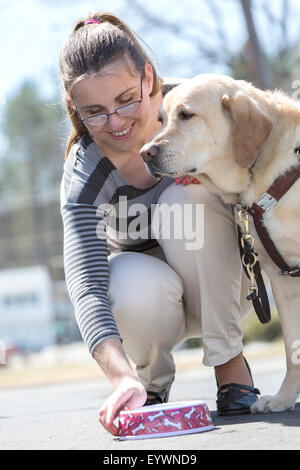 Jeune femme ayant une déficience visuelle nourrir son chien aidant Banque D'Images