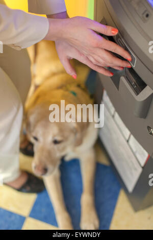 Jeune femme aveugle à l'aide d'un distributeur automatique de la banque avec son chien aidant l'attente Banque D'Images