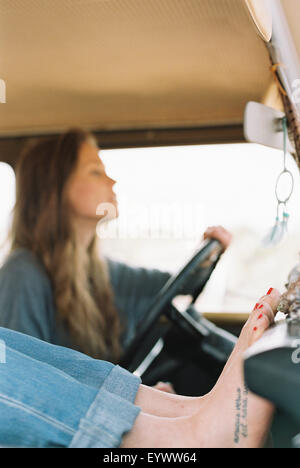 Femme aux pieds nus reposant ses pieds sur le tableau de bord d'un 4x4, un tatouage sur son pied droit, une autre femme au volant. Banque D'Images