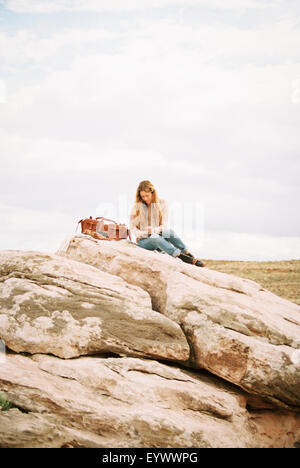 Femme assise sur un rocher avec sac en cuir Banque D'Images