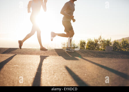 Portrait de deux personnes s'exécutant sur route de campagne au lever du soleil. Cropped shot of young man and woman jogging en matinée, avec br Banque D'Images