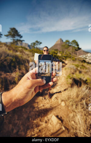 Man talking pictures of a man with mobile phone. se concentrer sur smart phone et de la main. Couple sur la randonnée dans la campagne. Banque D'Images