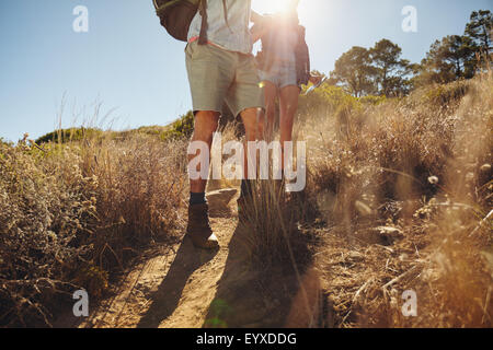 Low angle view of man and woman hikers walking on dirt trail sur la montagne sur une journée ensoleillée. Deux randonnées dans la nature. Banque D'Images