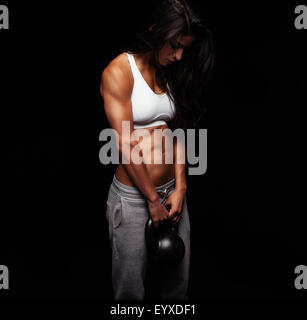 Jeune femme exerçant avec crossfit électrique poids bell. Les femmes travaillant hors du Crossfit sur fond noir. Banque D'Images