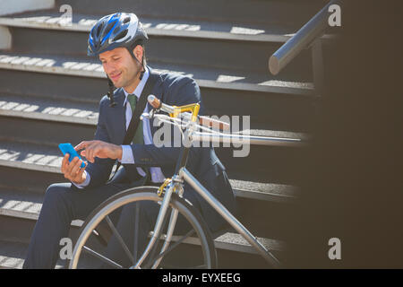 Man in suit avec Vélo et casque texting with cell phone on stairs Banque D'Images