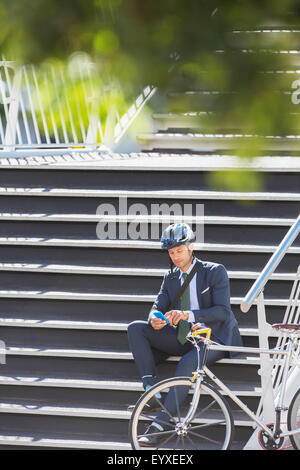 Businessman avec casque et location texting with cell phone on urban stairs Banque D'Images