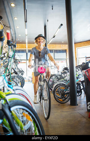 Smiling woman riding bicycle in bike shop Banque D'Images