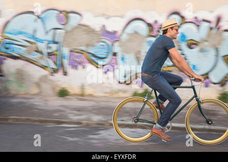 Hipster man riding bicycle sur route le long mur de graffiti urbain Banque D'Images