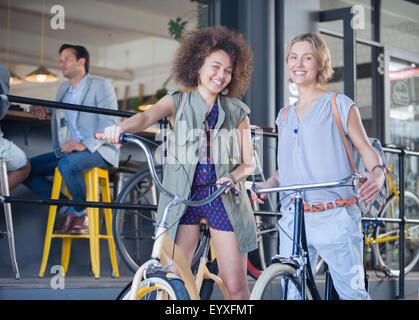 Portrait smiling women sur les bicyclettes café à l'extérieur Banque D'Images