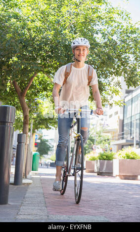Jeune femme avec casque riding bicycle in urban park Banque D'Images