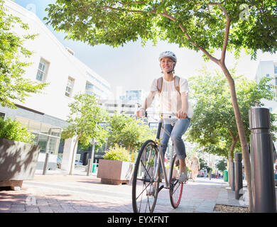 Smiling young woman with helmet riding bicycle in urban park Banque D'Images